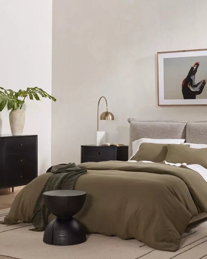 Black end table with single drawer and curved pedestal base in bedroom setting.
