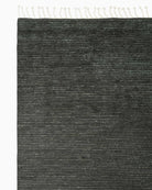 Dark gray textured rug with cream fringe trim on top and side edges.