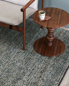 Teal and cream textured wool rug with wooden furniture and coffee cup on side table.