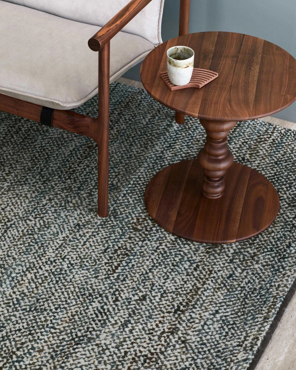 Teal and cream textured wool rug with wooden furniture and coffee cup on side table.