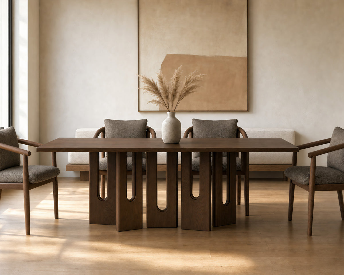 A modern dining table with a dark wood top and sculptural cutout legs, surrounded by four upholstered dining chairs in a warm, minimalist dining room setting.