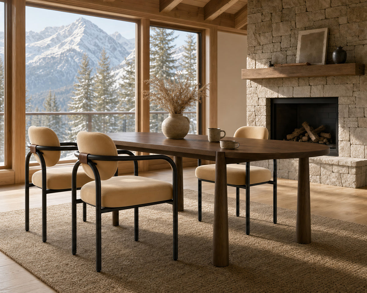 A dining set featuring a rectangular dark wood table and four matching armchairs with cream cushions and black metal frames, styled in a rustic cabin dining room with a stone fireplace and mountain views.