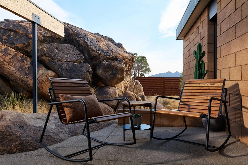 Outdoor patio area with Outdoor Strata Rockers, a table, and large rocks in the background.